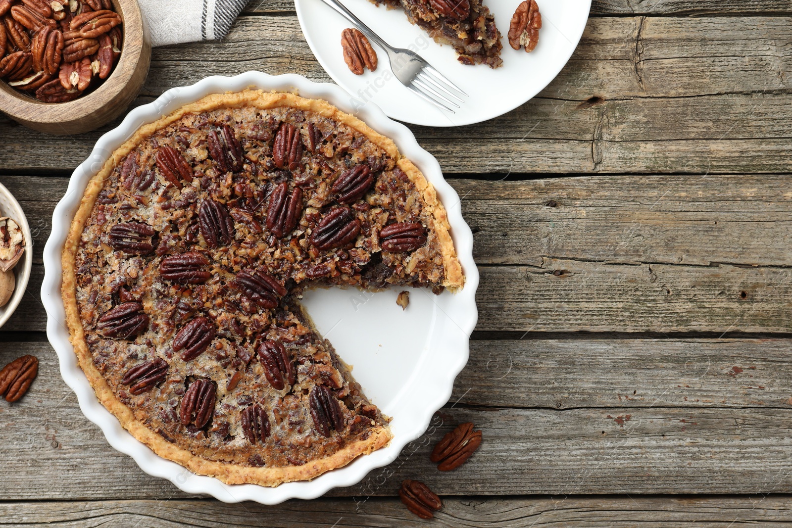 Photo of Delicious pecan pie in baking dish and fresh nuts on wooden table, flat lay. Space for text