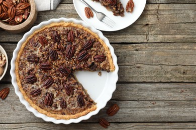 Photo of Delicious pecan pie in baking dish and fresh nuts on wooden table, flat lay. Space for text