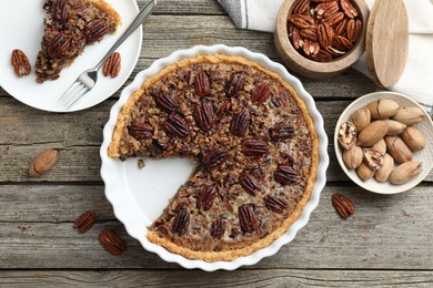 Photo of Delicious pecan pie in baking dish and fresh nuts on wooden table, flat lay