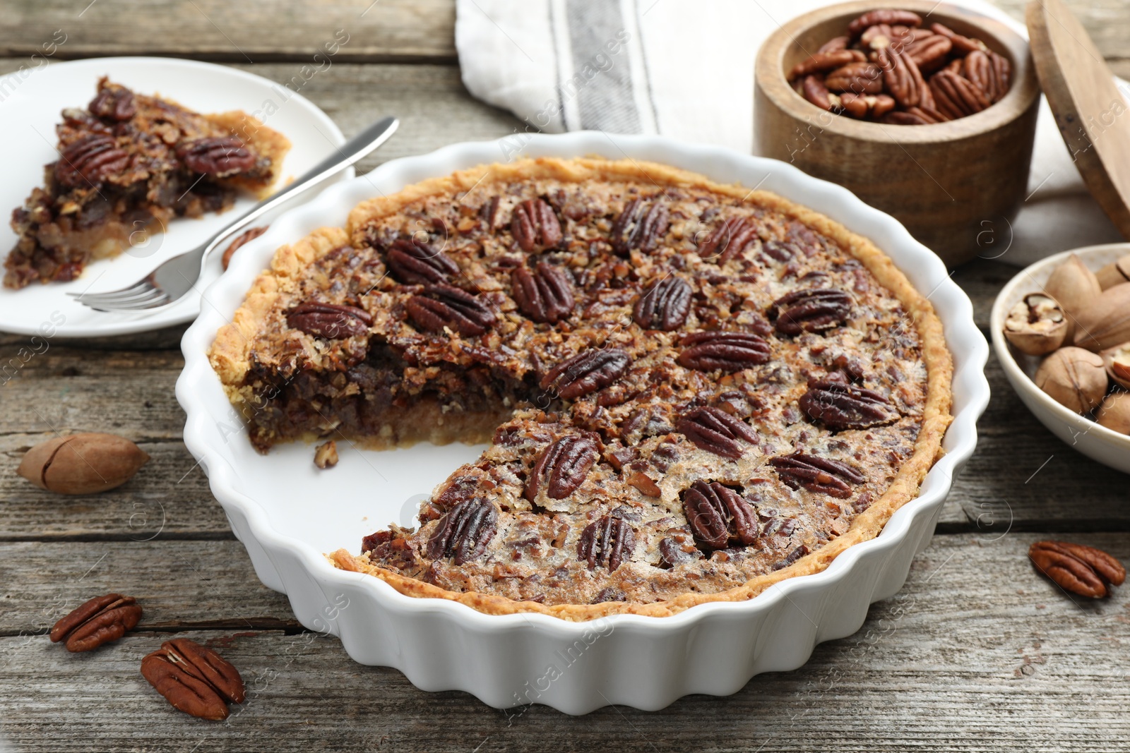 Photo of Delicious pecan pie in baking dish and fresh nuts on wooden table, closeup