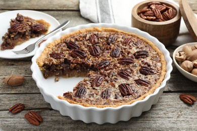 Delicious pecan pie in baking dish and fresh nuts on wooden table, closeup