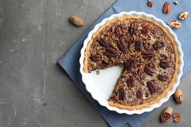 Photo of Delicious pecan pie in baking dish and fresh nuts on gray textured table, top view. Space for text