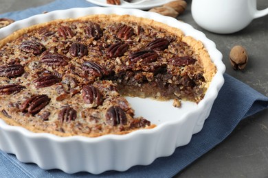 Photo of Delicious pecan pie in baking dish on gray textured table, closeup