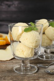 Photo of Scoops of melon sorbet and mint in glass dessert bowls on wooden table, closeup