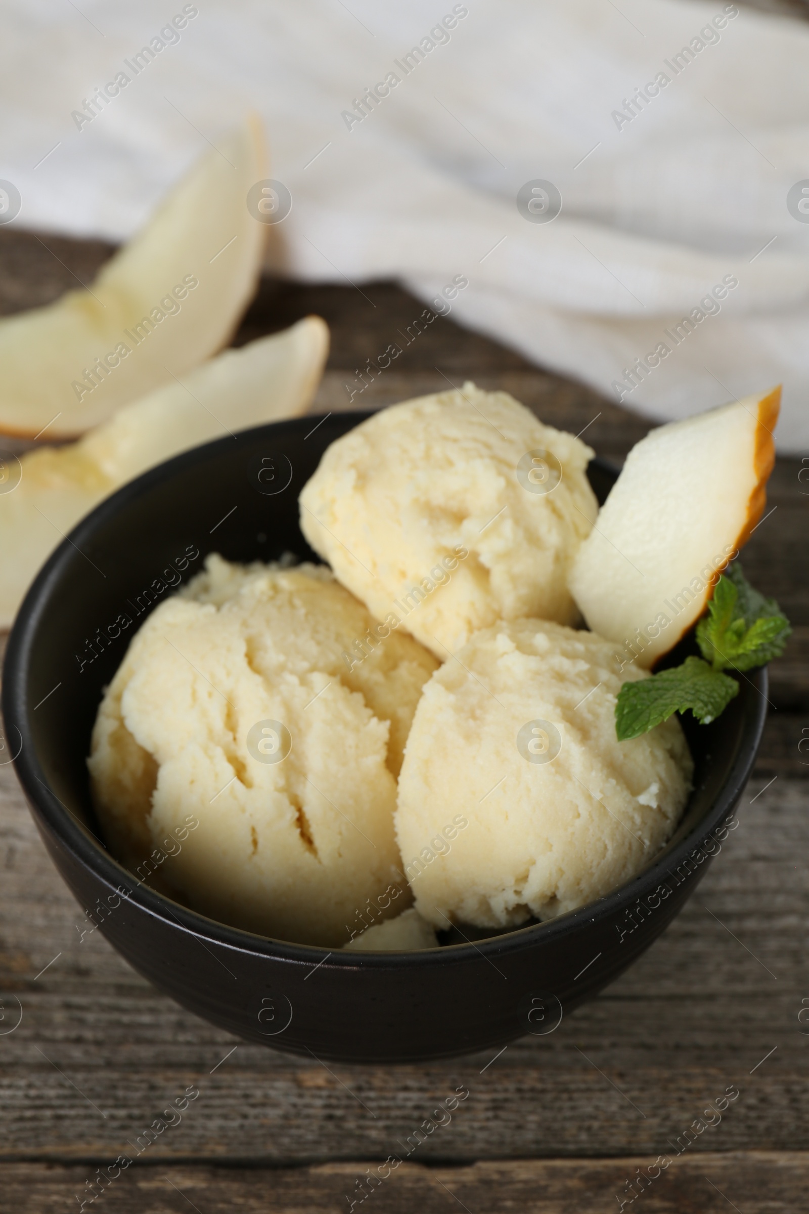 Photo of Scoops of melon sorbet with mint and fresh fruit in bowl on wooden table, closeup