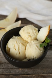 Scoops of melon sorbet with mint and fresh fruit in bowl on wooden table, closeup