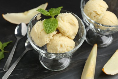 Photo of Scoops of melon sorbet with mint in glass dessert bowls, fresh fruit and spoons on dark table, closeup