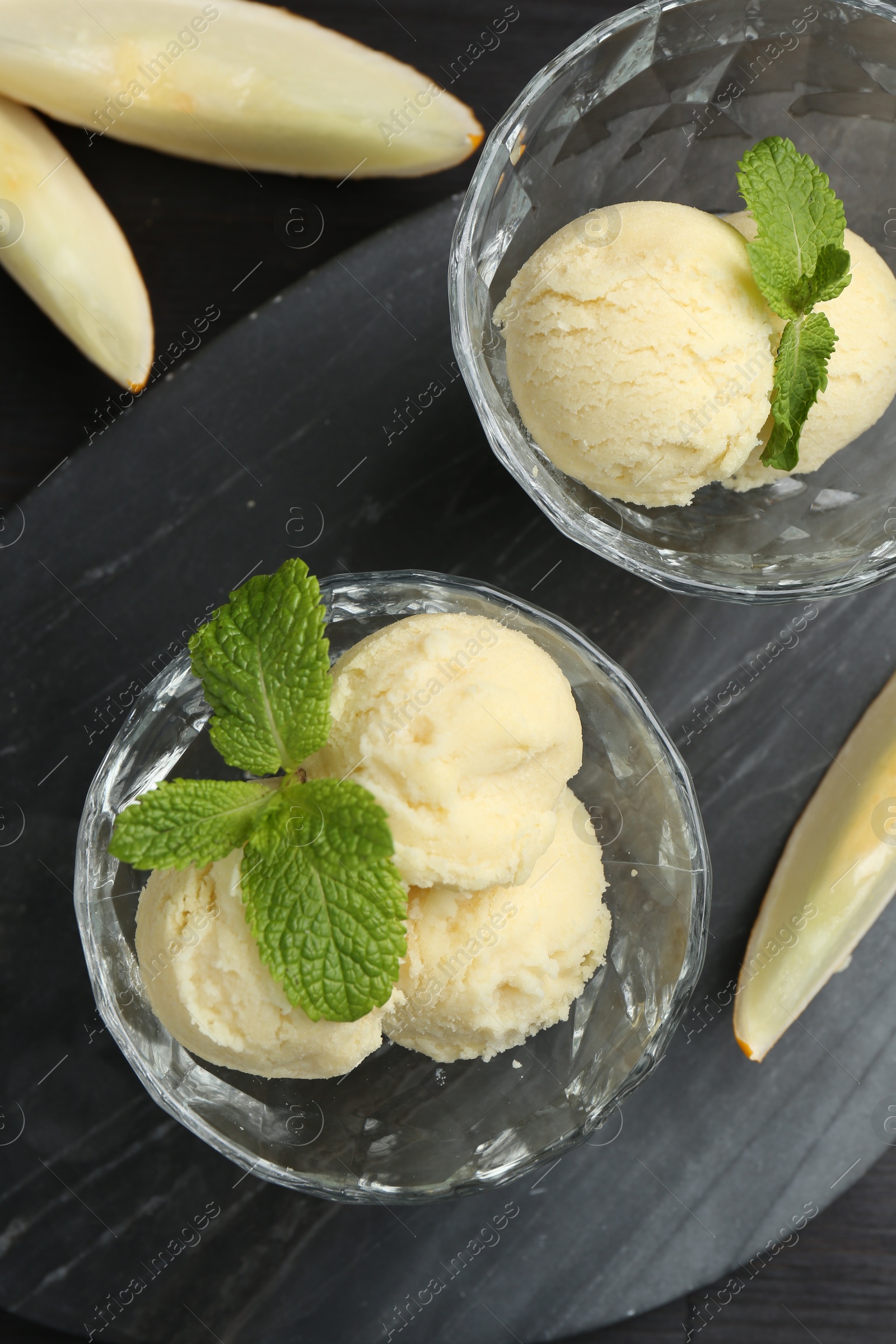 Photo of Scoops of melon sorbet with mint in glass dessert bowls and fresh fruit on dark wooden table, flat lay