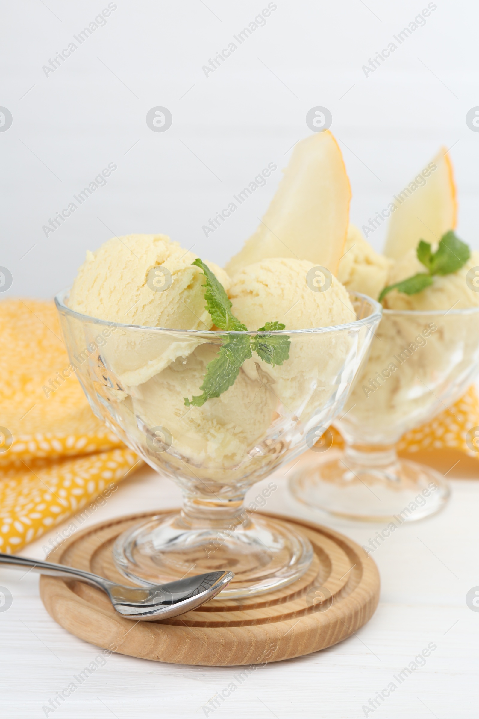 Photo of Scoops of melon sorbet with mint in glass dessert bowls and spoon on white wooden table, closeup