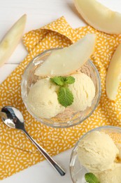 Scoops of melon sorbet with mint in glass dessert bowls, fresh fruit and spoon on white wooden table, flat lay