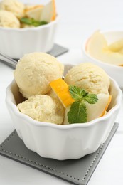 Scoops of melon sorbet with mint and fresh fruit in bowls on white wooden table, closeup