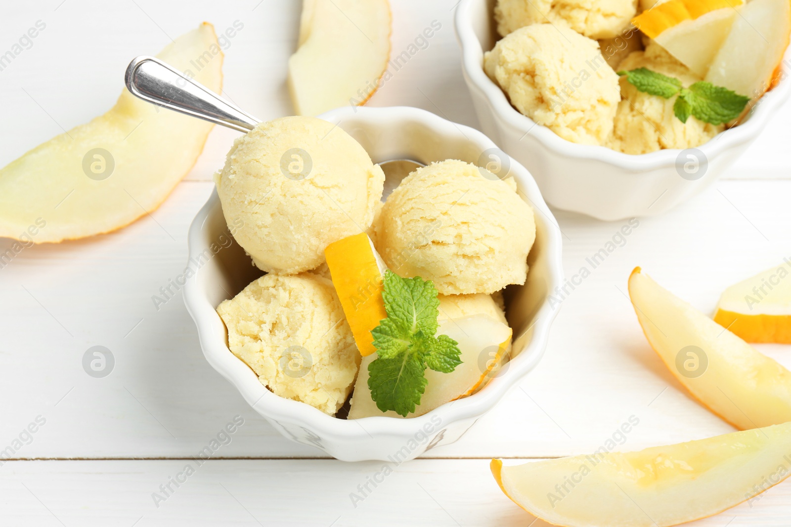 Photo of Scoops of melon sorbet with mint and fresh fruit in bowls on white wooden table, above view