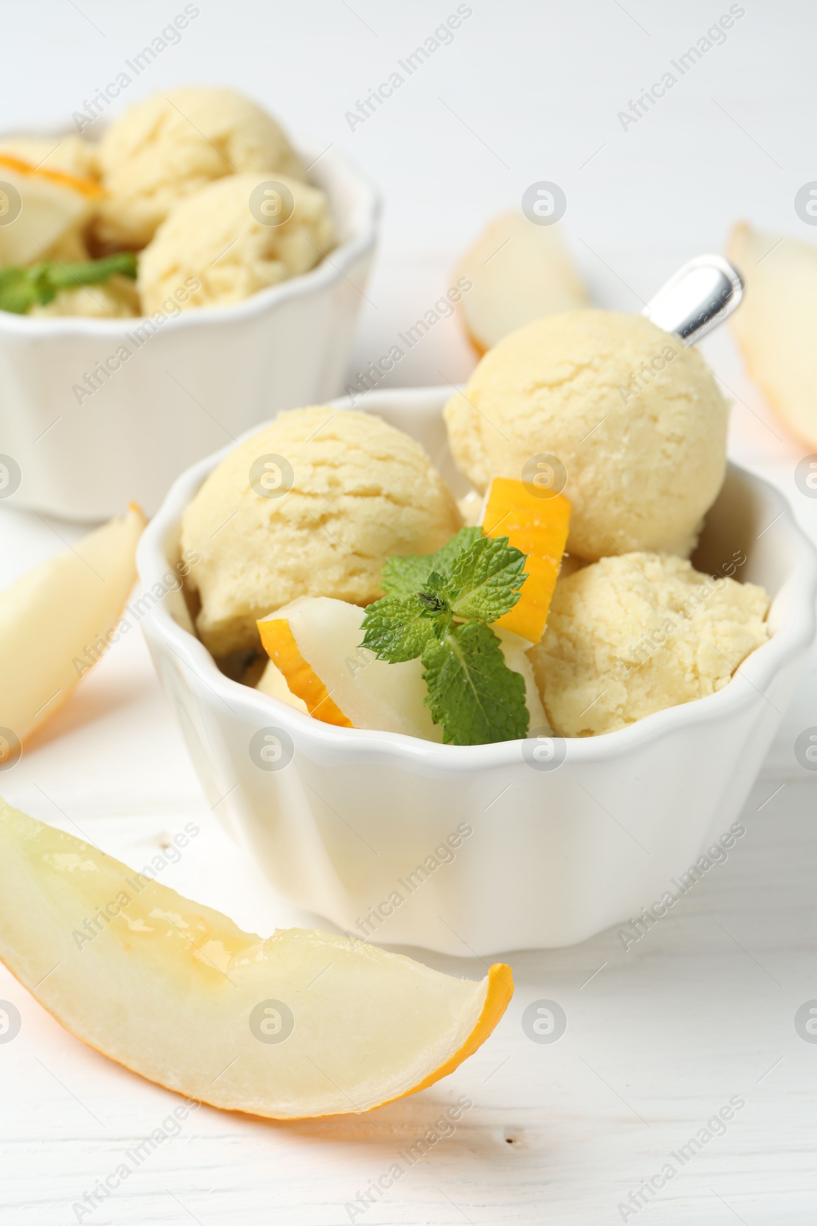 Photo of Scoops of melon sorbet with mint and fresh fruit in bowls on white wooden table, closeup