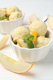 Scoops of melon sorbet with mint and fresh fruit in bowls on white wooden table, closeup