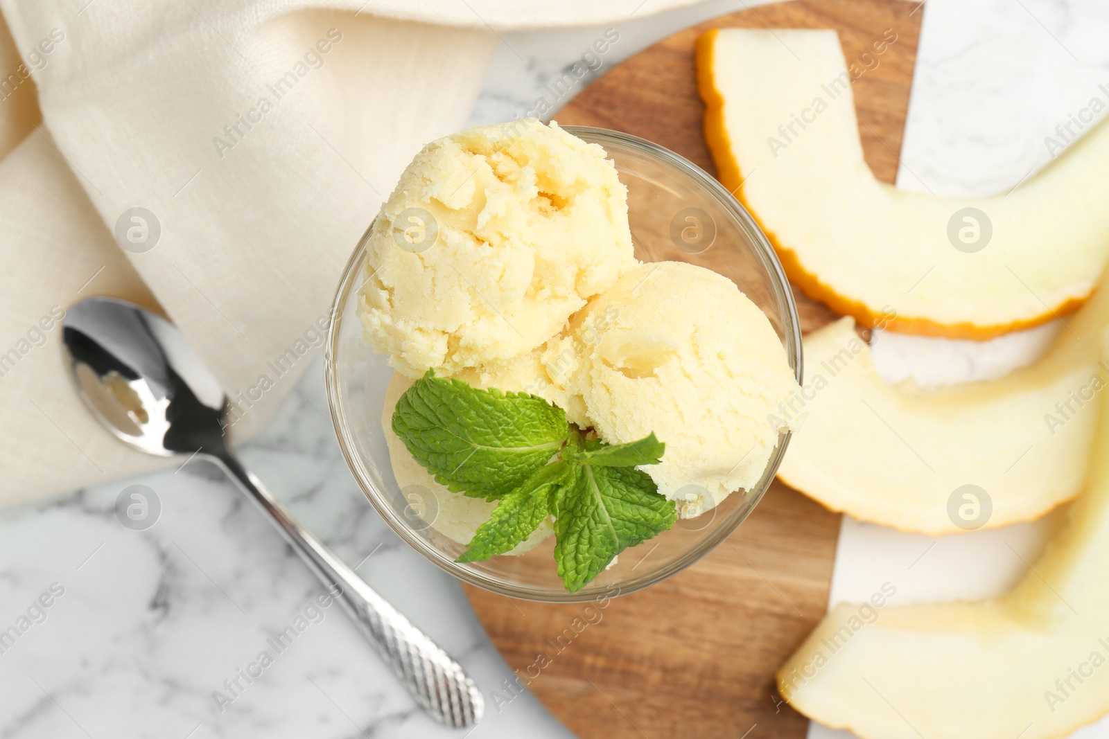 Photo of Scoops of melon sorbet with mint in glass dessert bowl and fresh fruit on light marble table, flat lay