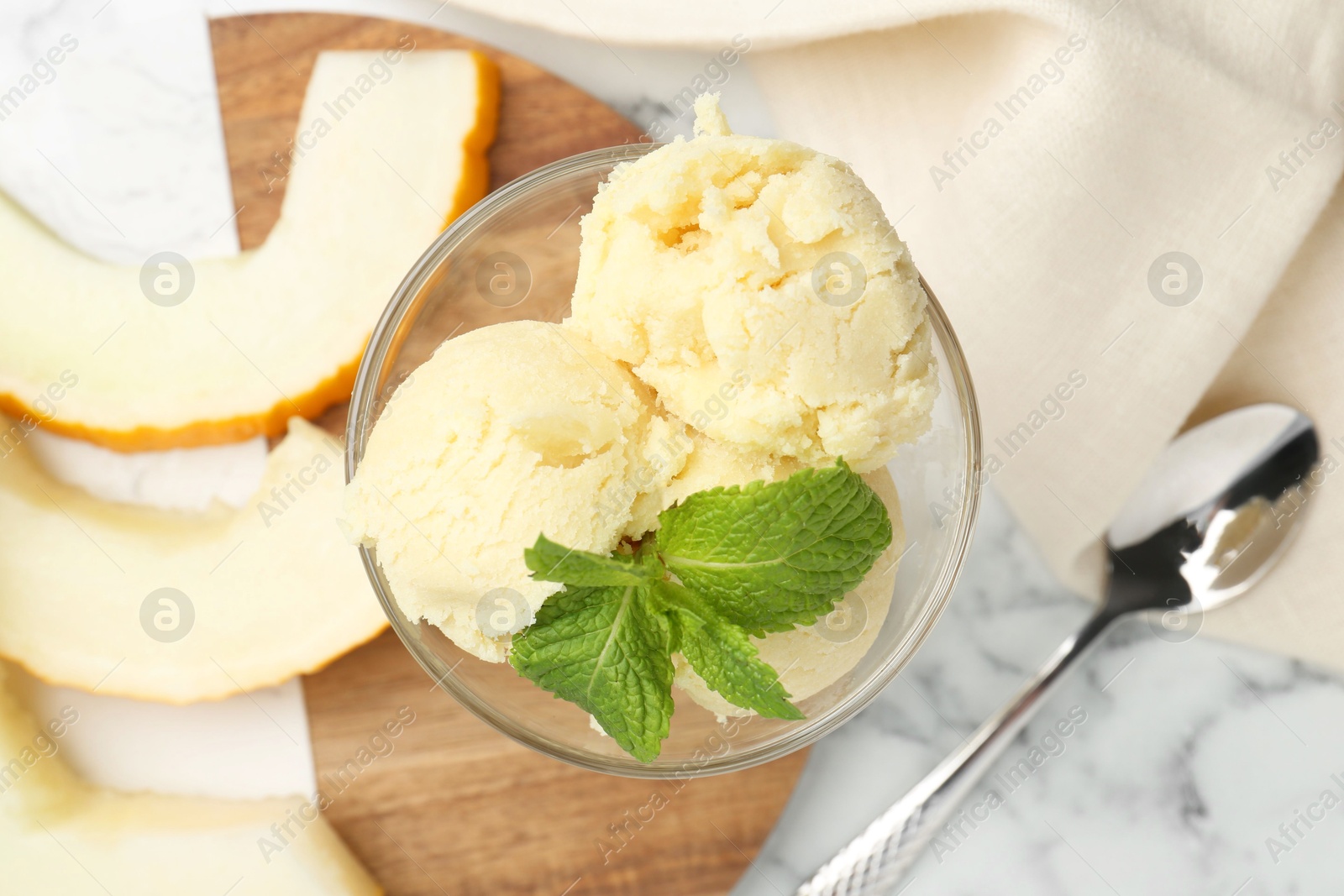 Photo of Scoops of melon sorbet with mint in glass dessert bowl and fresh fruit on light marble table, flat lay