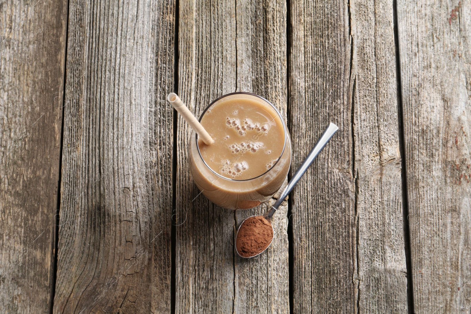 Photo of Delicious protein shake in glass and spoon with powder on wooden table, top view