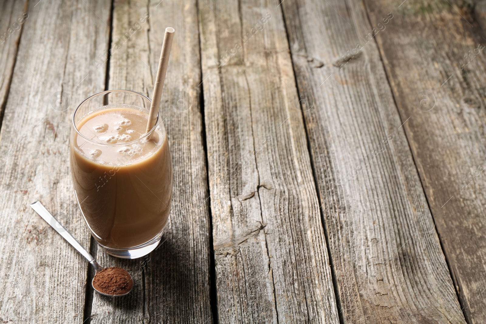 Photo of Delicious protein shake in glass and spoon with powder on wooden table, space for text