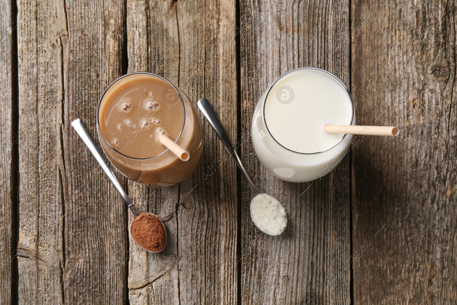 Photo of Delicious protein shakes in glasses and spoons with powder on wooden table, flat lay