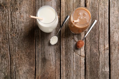 Photo of Delicious protein shakes in glasses and spoons with powder on wooden table, flat lay. Space for text