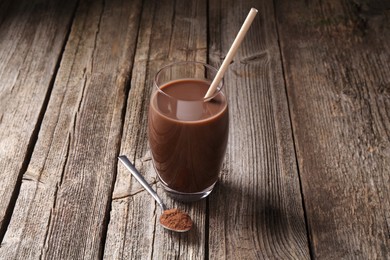 Photo of Delicious protein shake in glass and spoon with powder on wooden table