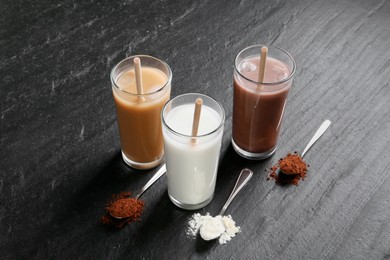 Photo of Delicious protein shakes in glasses and spoons with powder on black table