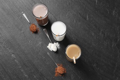 Photo of Delicious protein shakes in glasses and spoons with powder on black table, flat lay