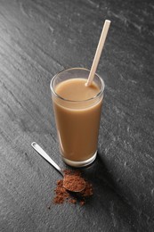 Photo of Delicious protein shake in glass and spoon with powder on black table