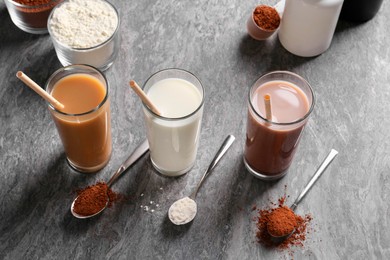 Photo of Delicious protein shakes in glasses, powder and spoons on grey table