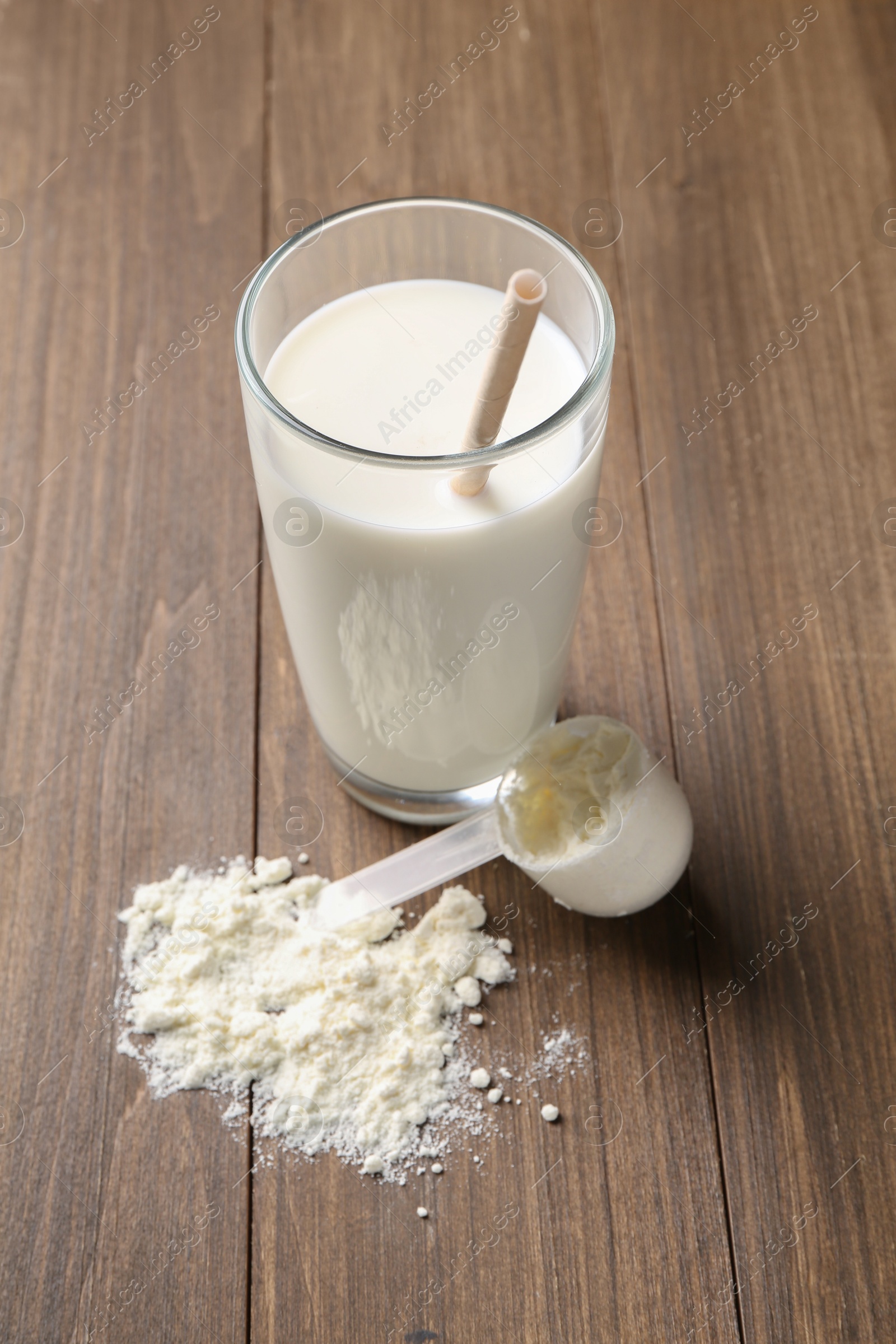 Photo of Delicious protein shake in glass, scoop and powder on wooden table