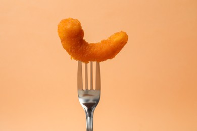 Photo of Fork with tasty fried shrimp on pale orange background, closeup