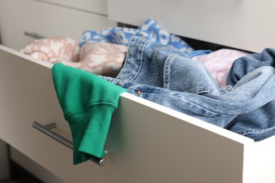 Cluttered chest of drawers indoors, closeup. Clothes in mess