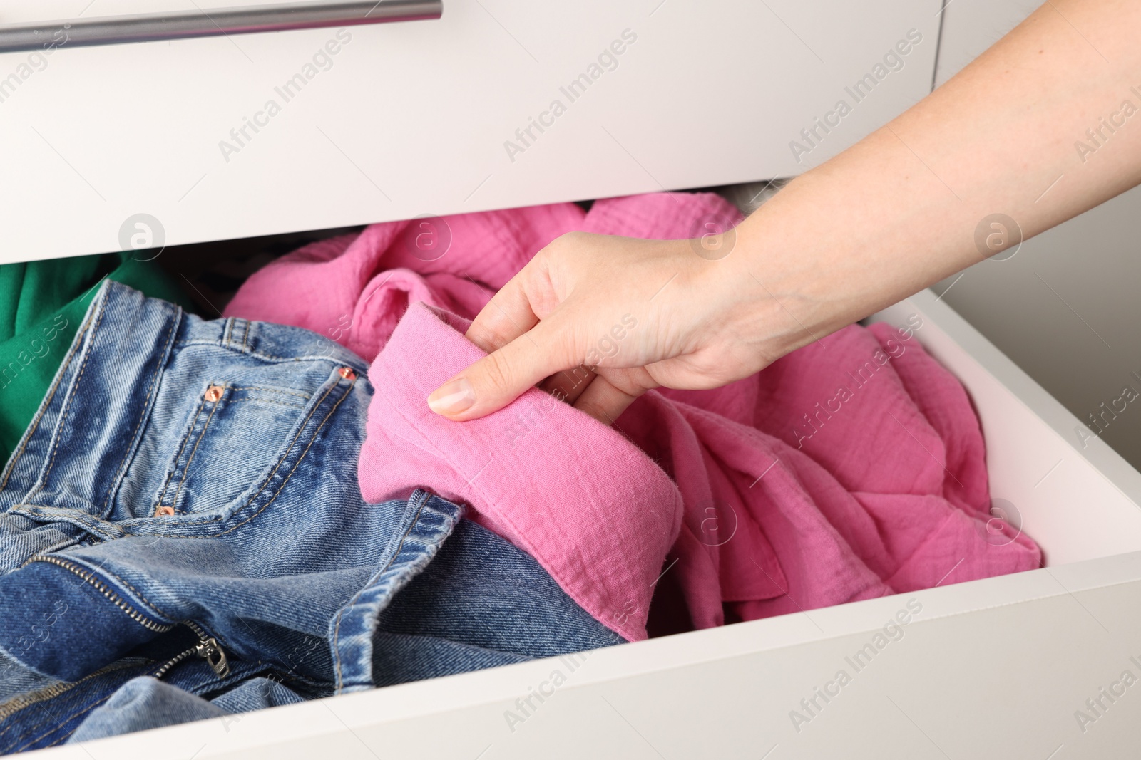 Photo of Woman organizing clothes in chest of drawers indoors, closeup