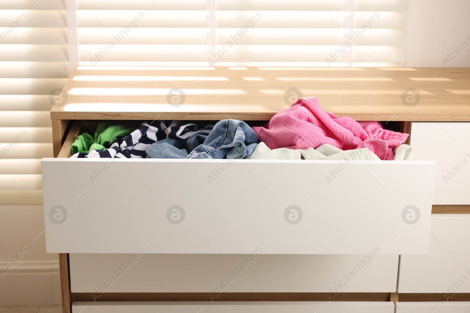 Photo of Cluttered chest of drawers indoors. Clothes in mess