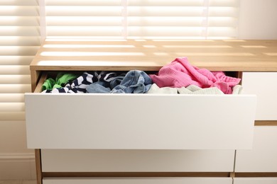 Photo of Cluttered chest of drawers indoors. Clothes in mess