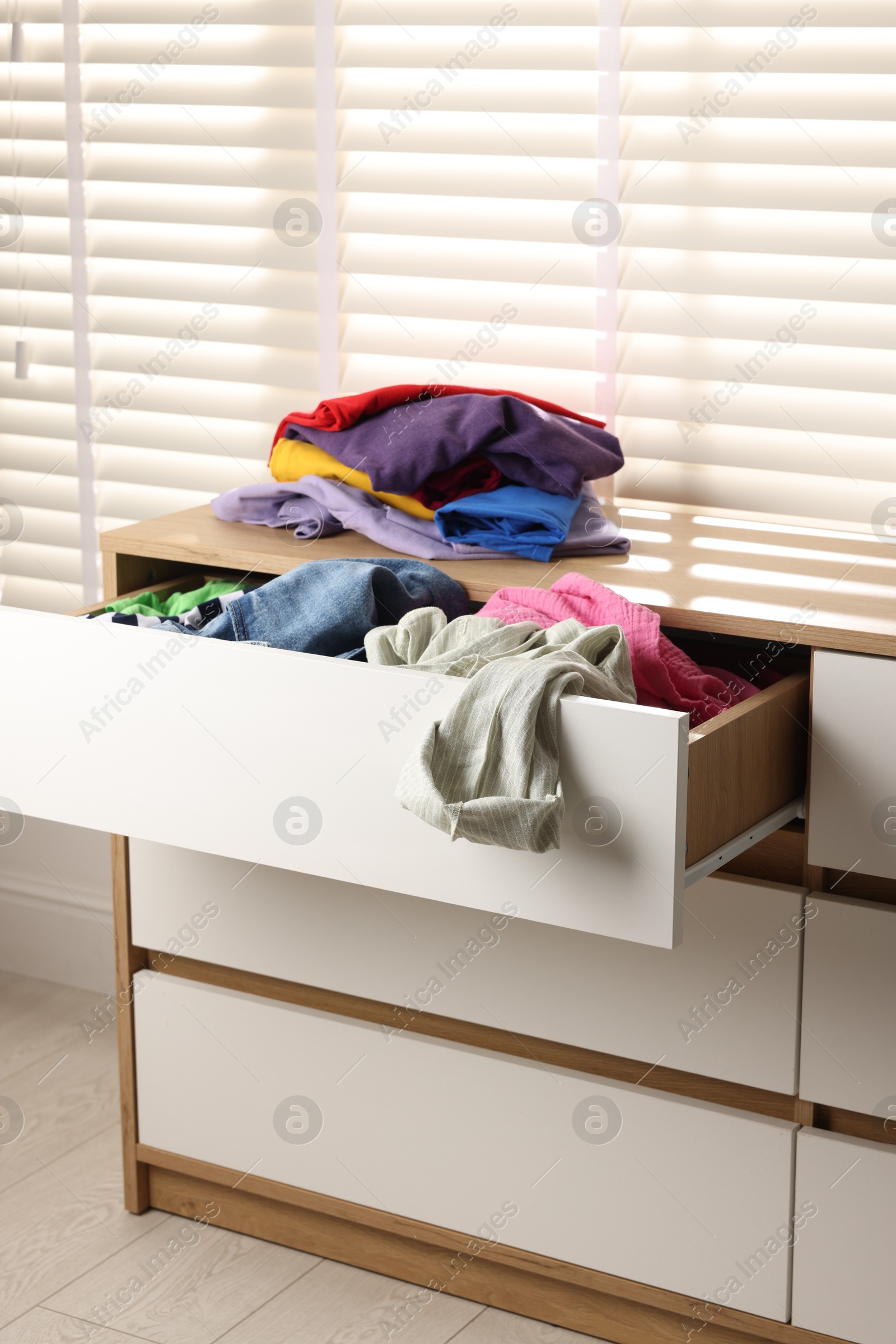 Photo of Cluttered chest of drawers indoors. Clothes in mess