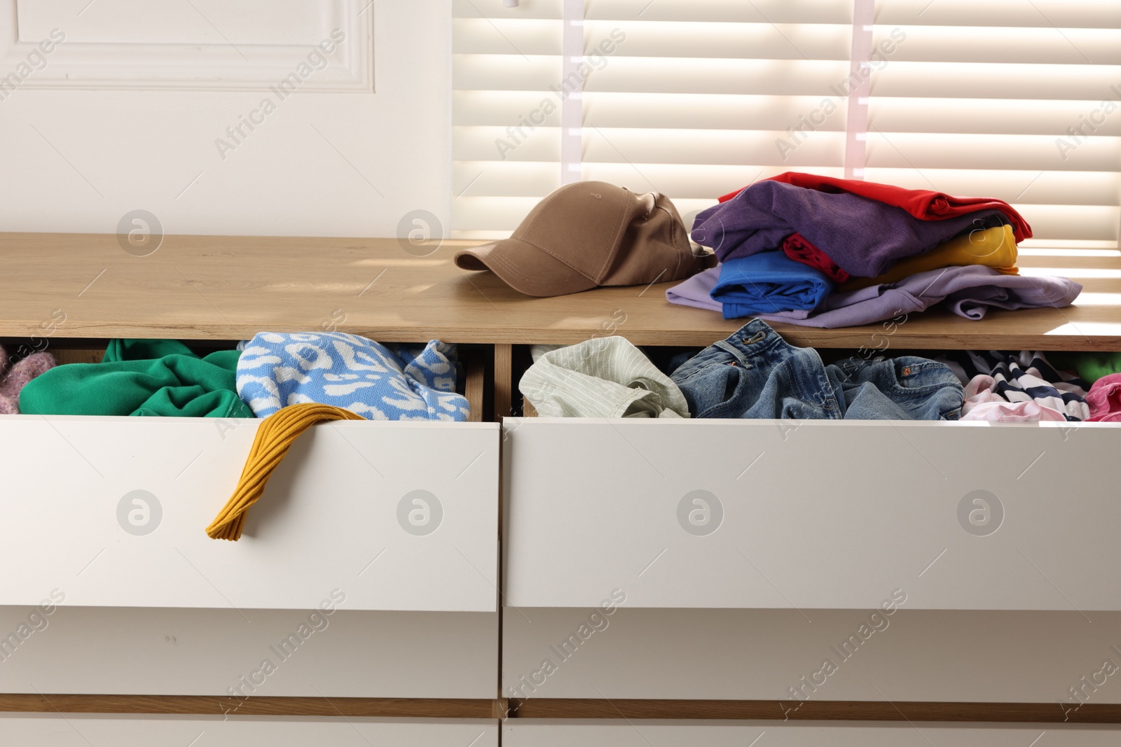 Photo of Cluttered chest of drawers indoors, closeup. Clothes in mess