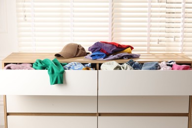 Cluttered chest of drawers indoors, closeup. Clothes in mess