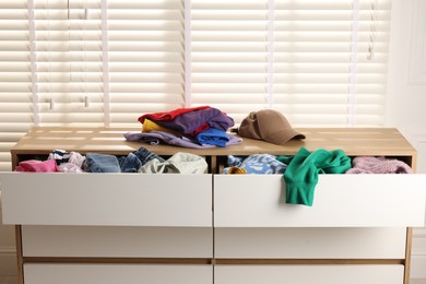 Photo of Cluttered chest of drawers indoors, closeup. Clothes in mess