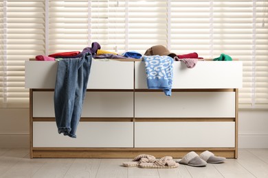 Photo of Cluttered chest of drawers indoors. Clothes in mess