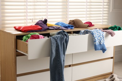 Photo of Cluttered chest of drawers indoors. Clothes in mess