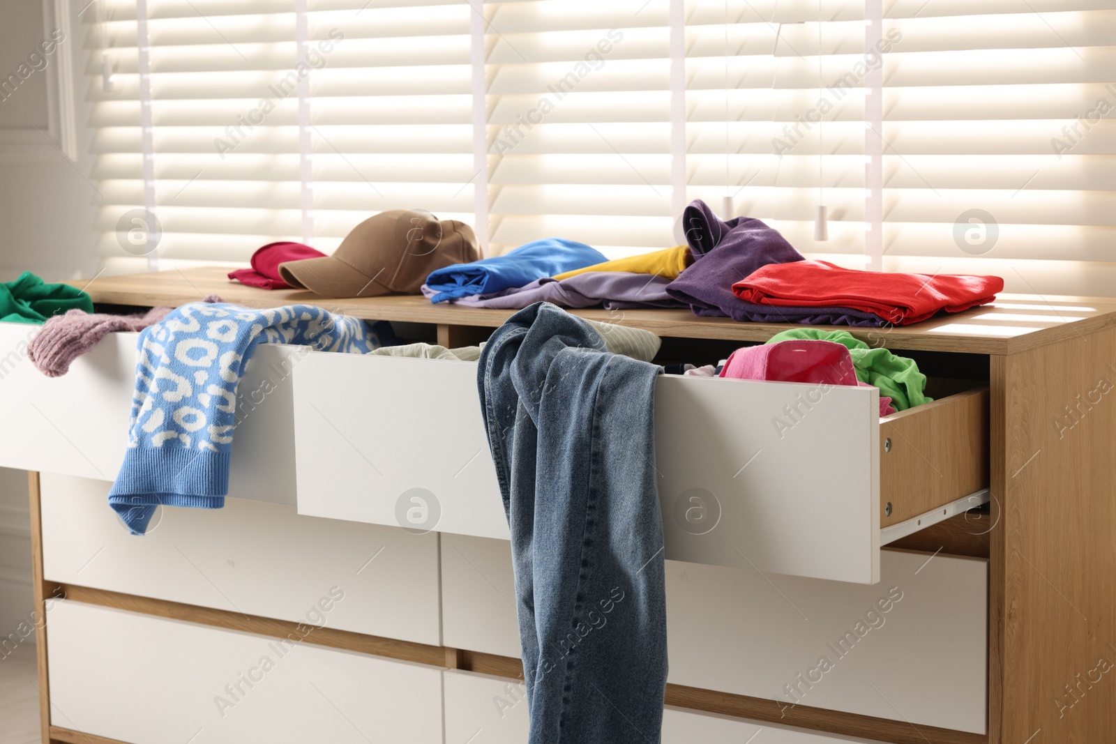 Photo of Cluttered chest of drawers indoors. Clothes in mess