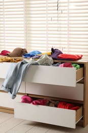 Photo of Cluttered chest of drawers indoors. Clothes in mess