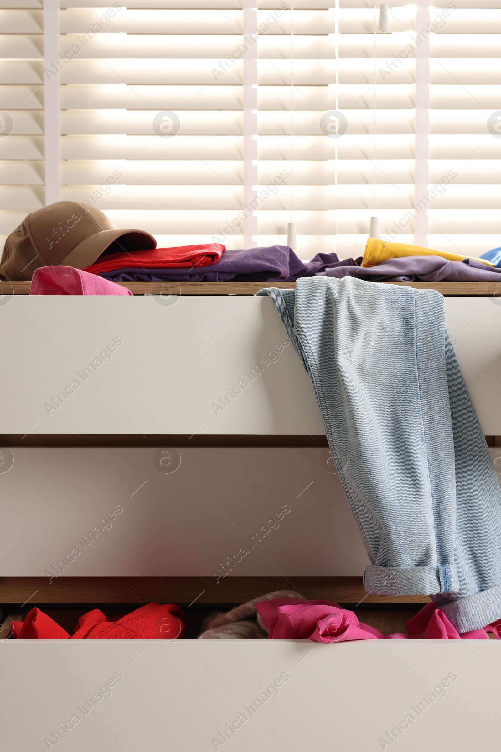 Photo of Cluttered chest of drawers indoors, closeup. Clothes in mess