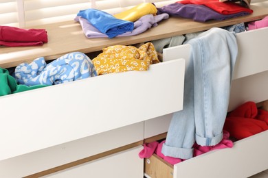 Photo of Cluttered chest of drawers indoors, closeup. Clothes in mess