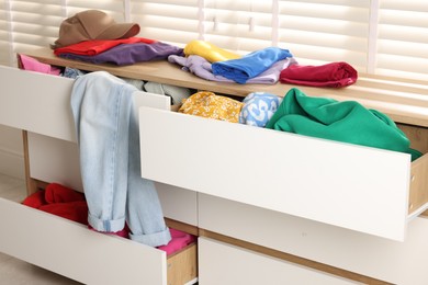 Cluttered chest of drawers indoors, closeup. Clothes in mess