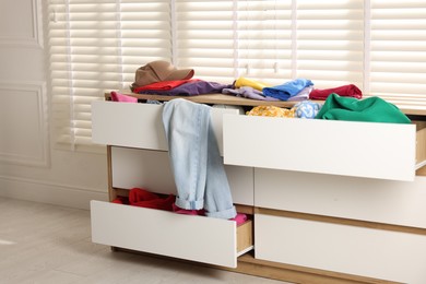 Photo of Cluttered chest of drawers indoors. Clothes in mess