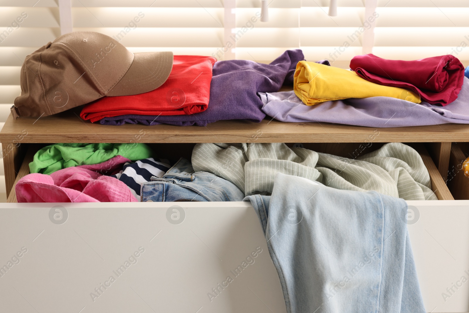 Photo of Cluttered chest of drawers indoors, closeup. Clothes in mess