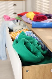 Cluttered chest of drawers indoors, closeup. Clothes in mess