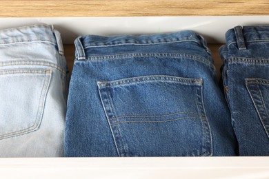 Photo of Chest of drawers with different folded jeans, closeup